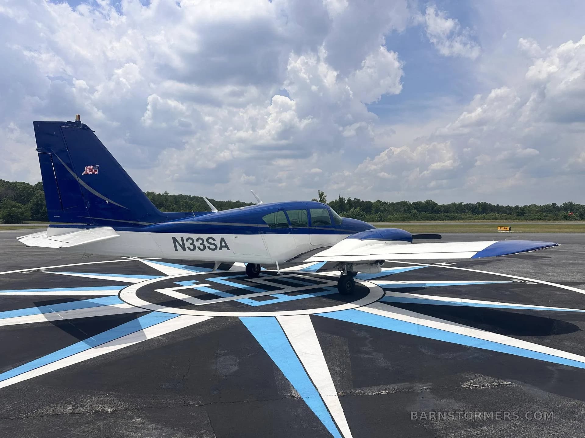 A side view of a blue and white single-engine aircraft (N33SA) parked on a compass rose marking on an airfield.