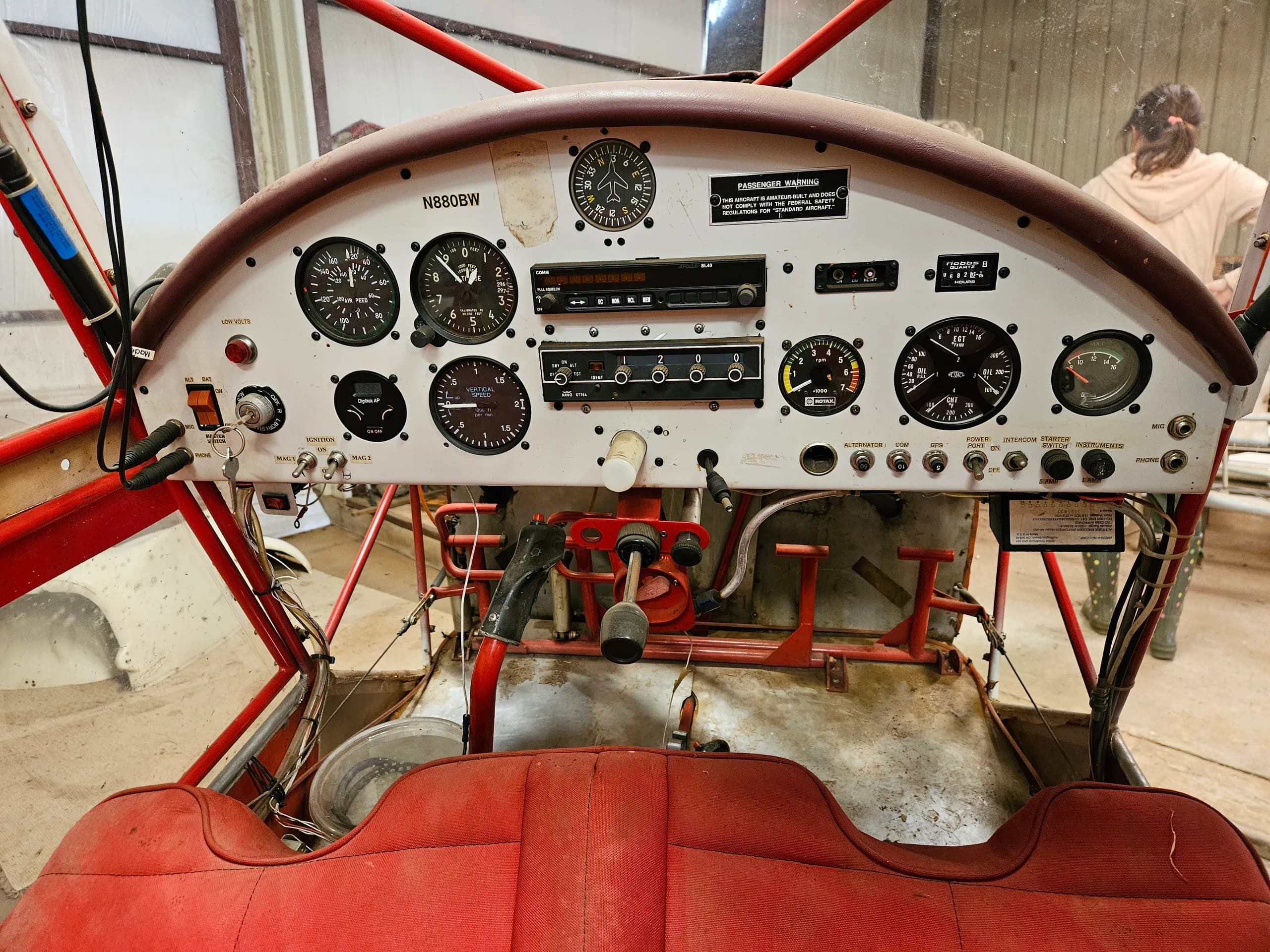 The cockpit of the N880BW experimental aircraft, showing the instrument panel with gauges, radio, and red upholstered seats.