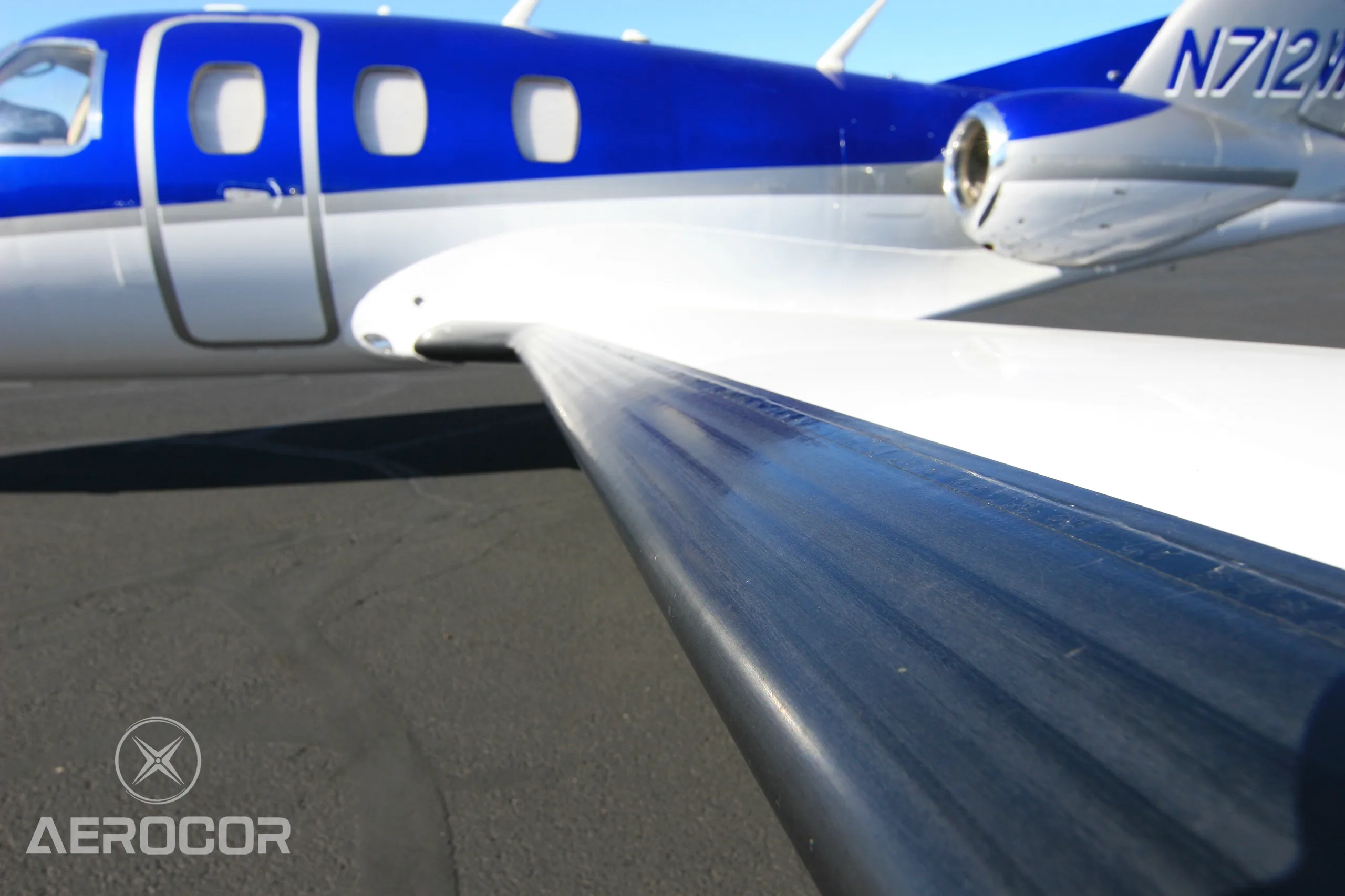 A close-up view of the wing and fuselage of the blue and white Eclipse 500/550 jet, N712WG.