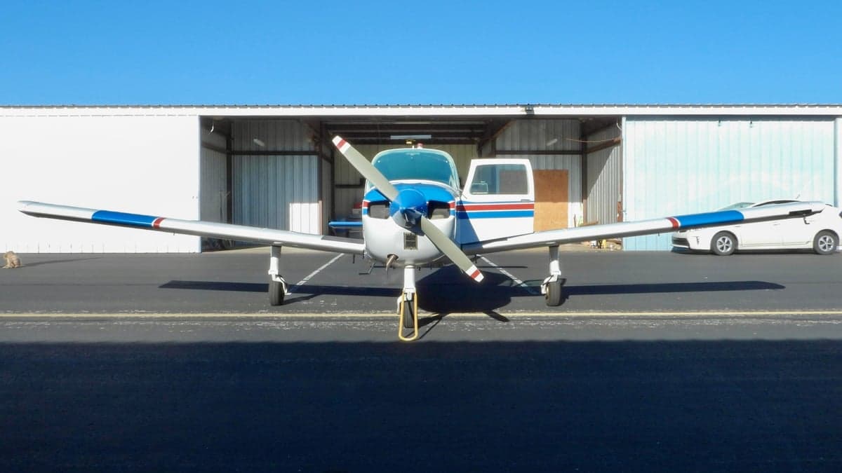 Front view of a blue and white Piper PA-28-140 Cherokee at an airport.