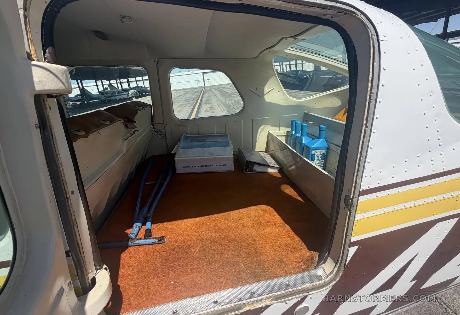 The open cargo door reveals the aircraft's interior with orange carpet and various items stored inside.