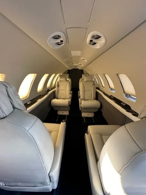 View of the aircraft cabin with white leather seats and window shades.