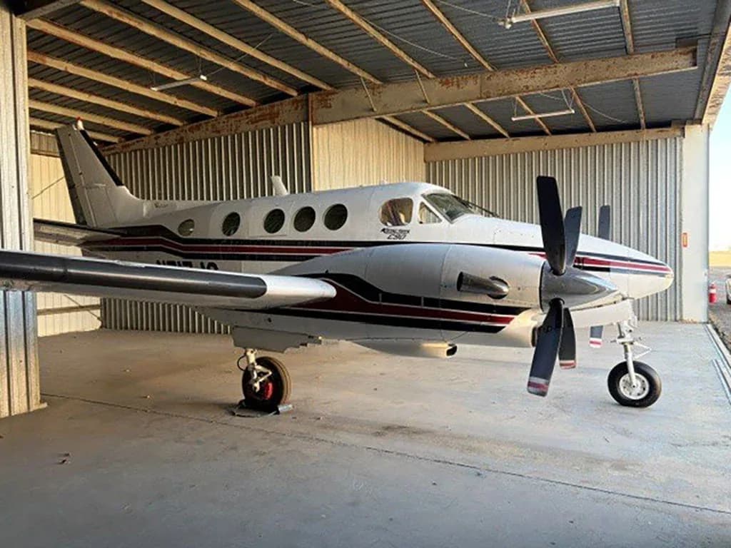 A white and red Beechcraft King Air C90 aircraft with registration N717JG parked in a hangar, viewed from the side.
