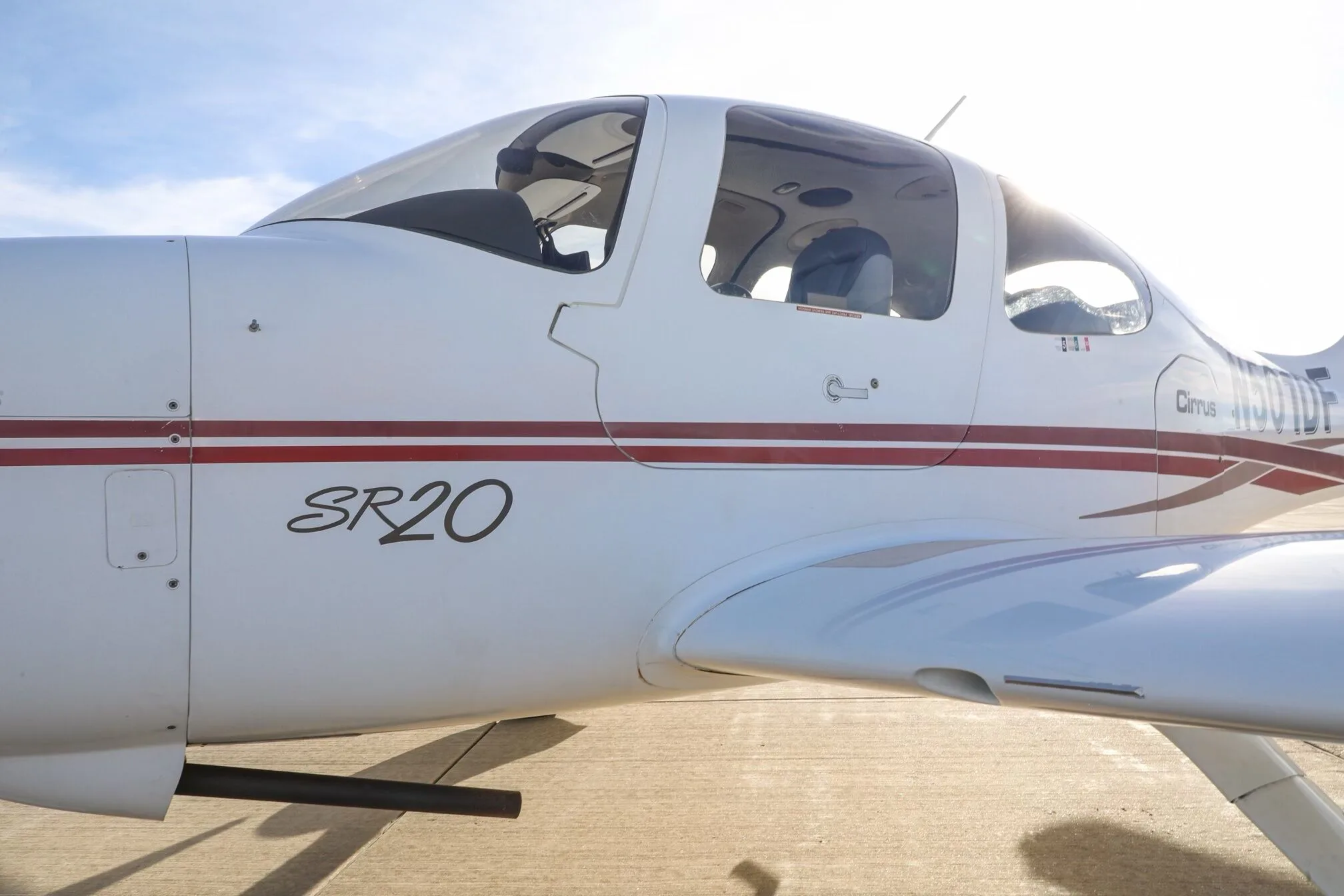 Close-up side view of the fuselage of a white Cirrus SR20 aircraft with red stripes.
