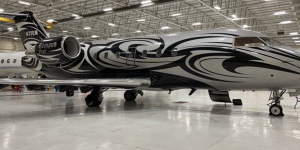 A Bombardier Challenger jet with a custom black and silver paint scheme is parked in a hangar.