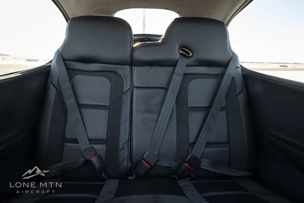 A closer view of the black leather rear seats with seatbelts in the aircraft cabin.