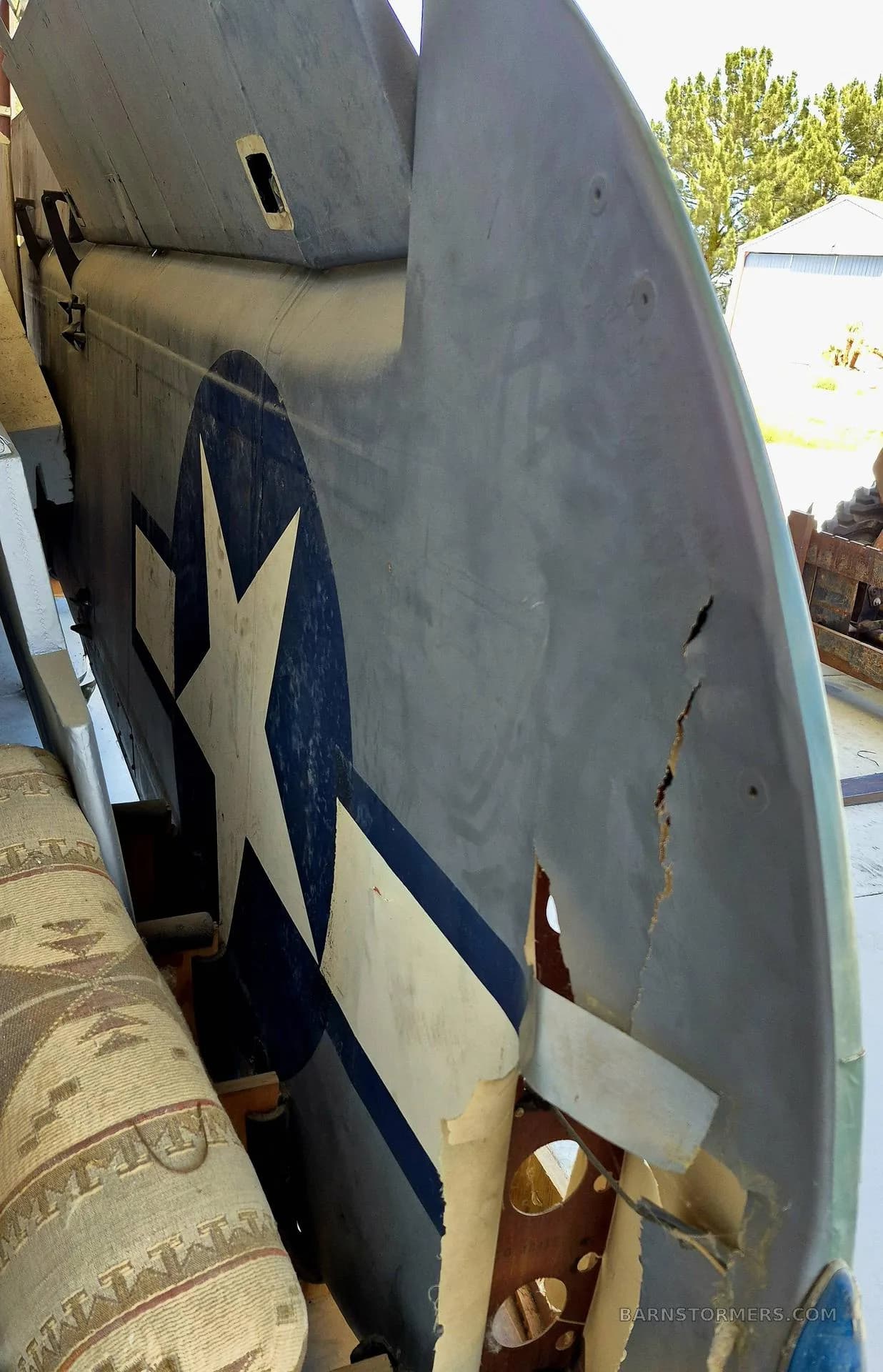 A damaged tail section of an aircraft, featuring a faded US star insignia, with exposed internal structure.