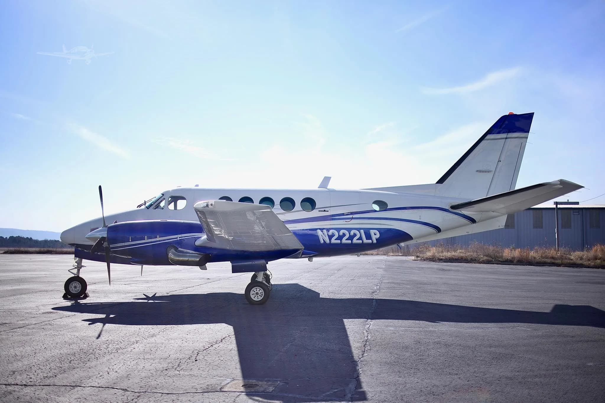 A white and blue twin-engine turboprop aircraft (Beechcraft King Air) with registration N222LP parked on an asphalt ramp under a clear sky.