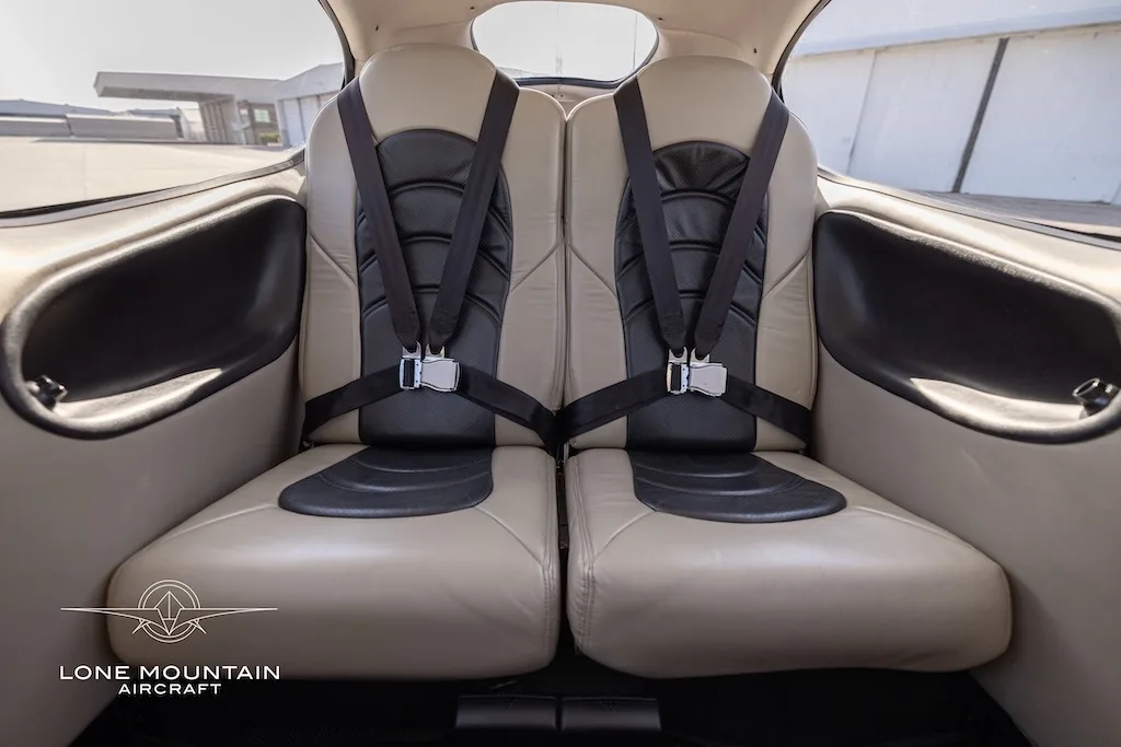 The tan and black leather rear seats of a Cirrus SR22 aircraft cabin, with seatbelts fastened.