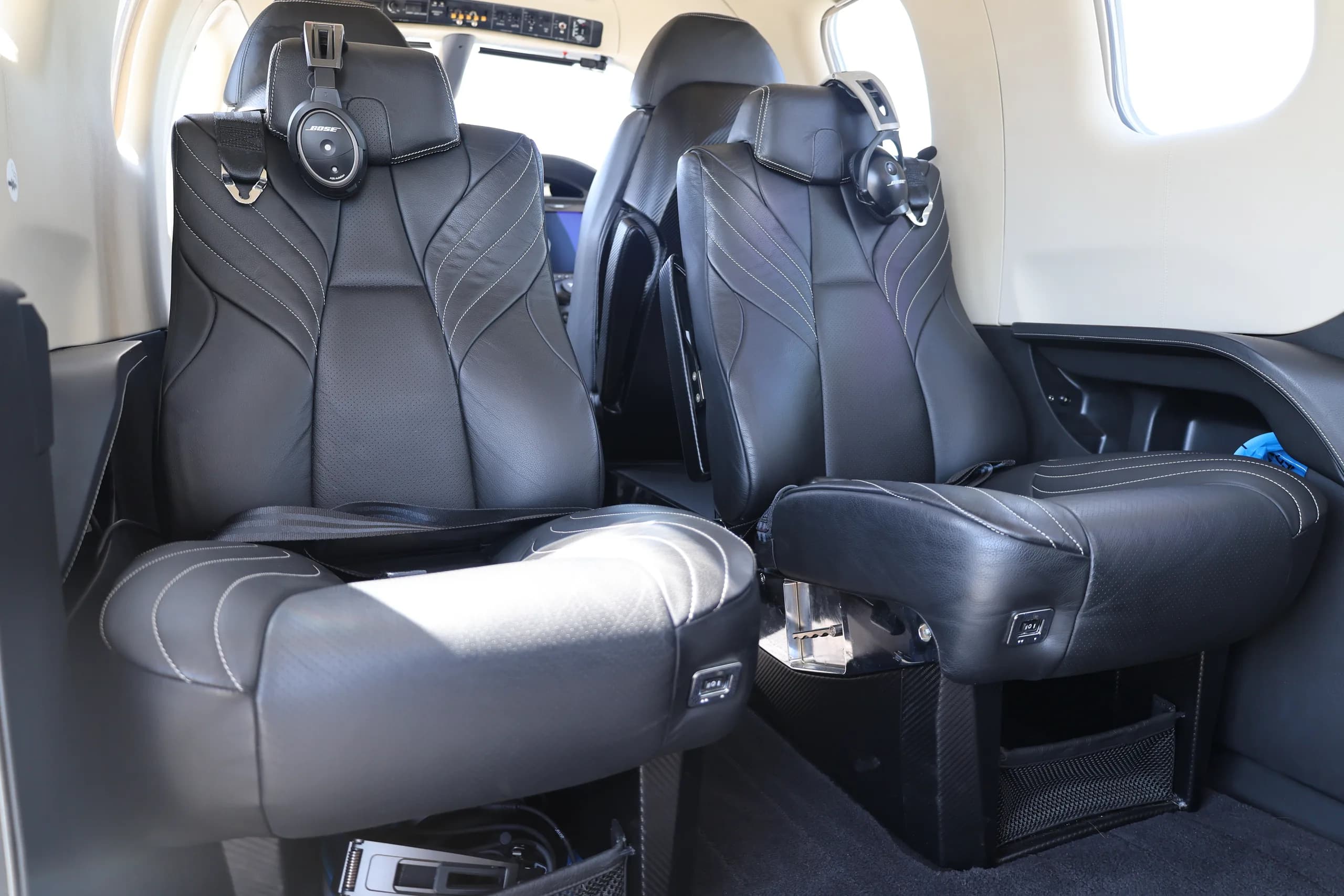 Two black leather passenger seats with headphones in the interior cabin of an aircraft.