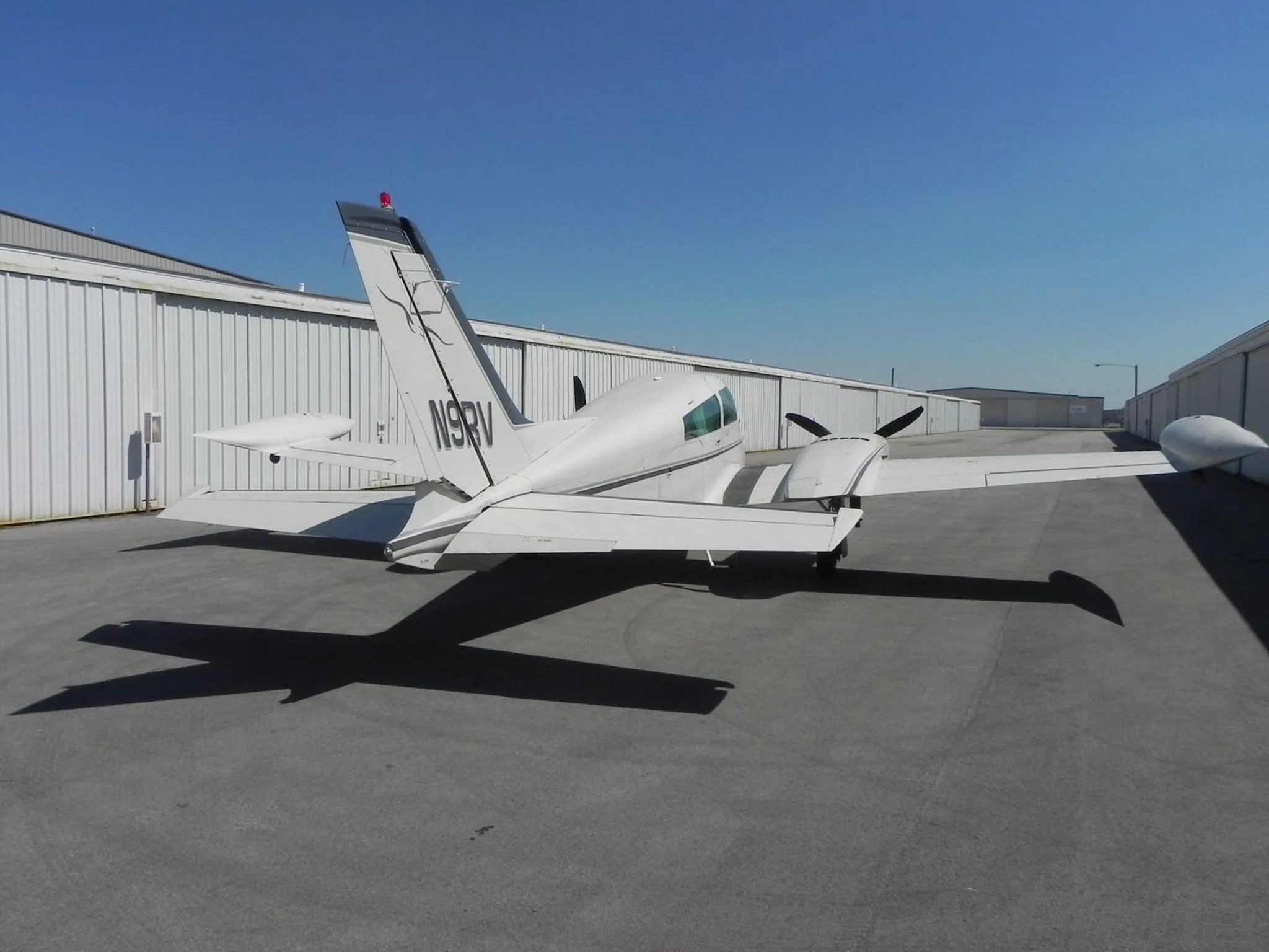 A rear three-quarter view of a white twin-engine Cessna 310 aircraft with tail number N9RV parked on an asphalt apron.