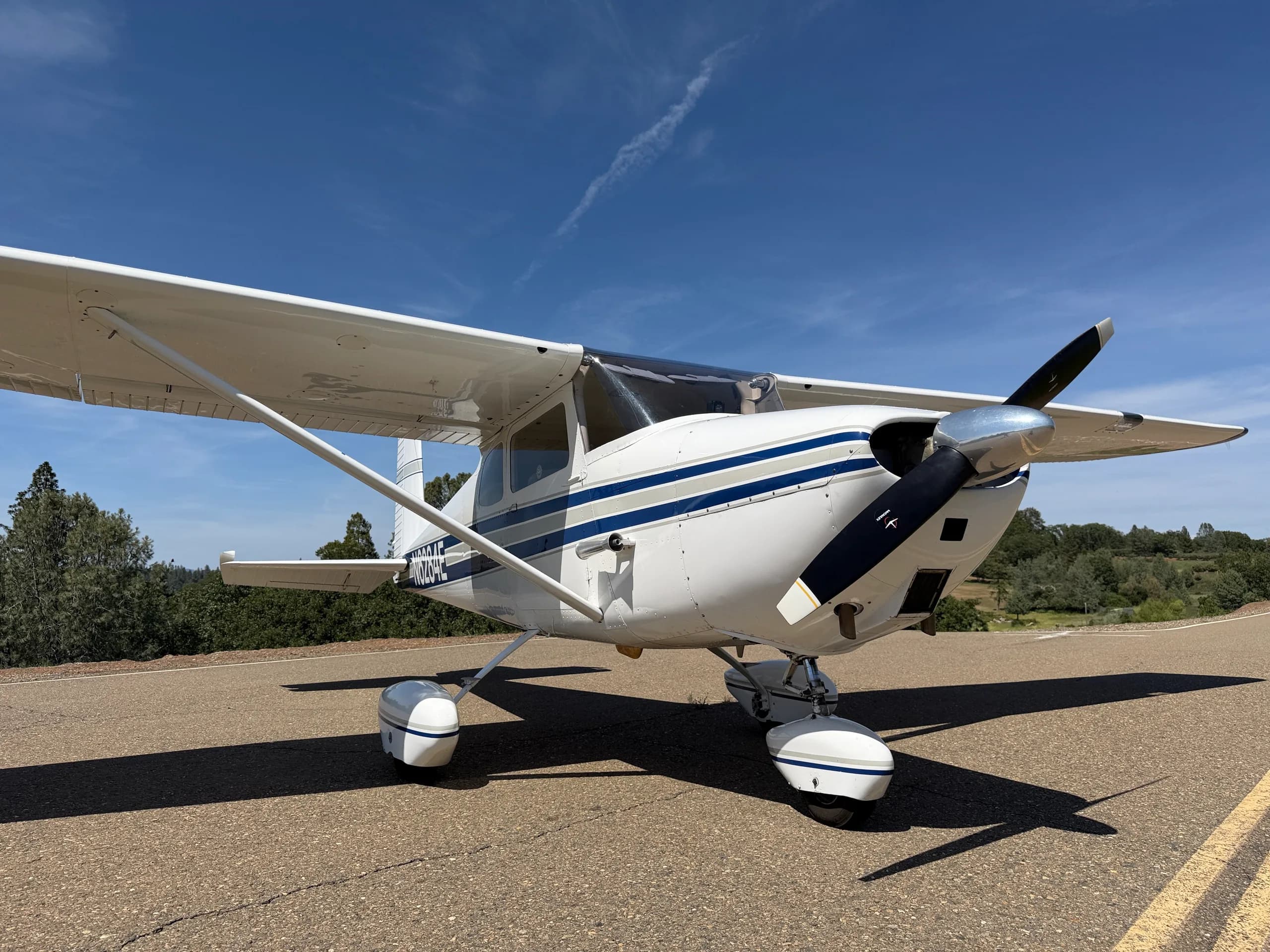 A low-angle front-quarter view of a white Cessna 172 with blue stripes, N6284E, on an asphalt road.