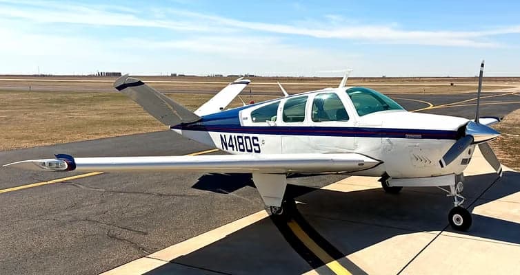 A Beechcraft Bonanza with a white and blue paint scheme is parked on the tarmac.