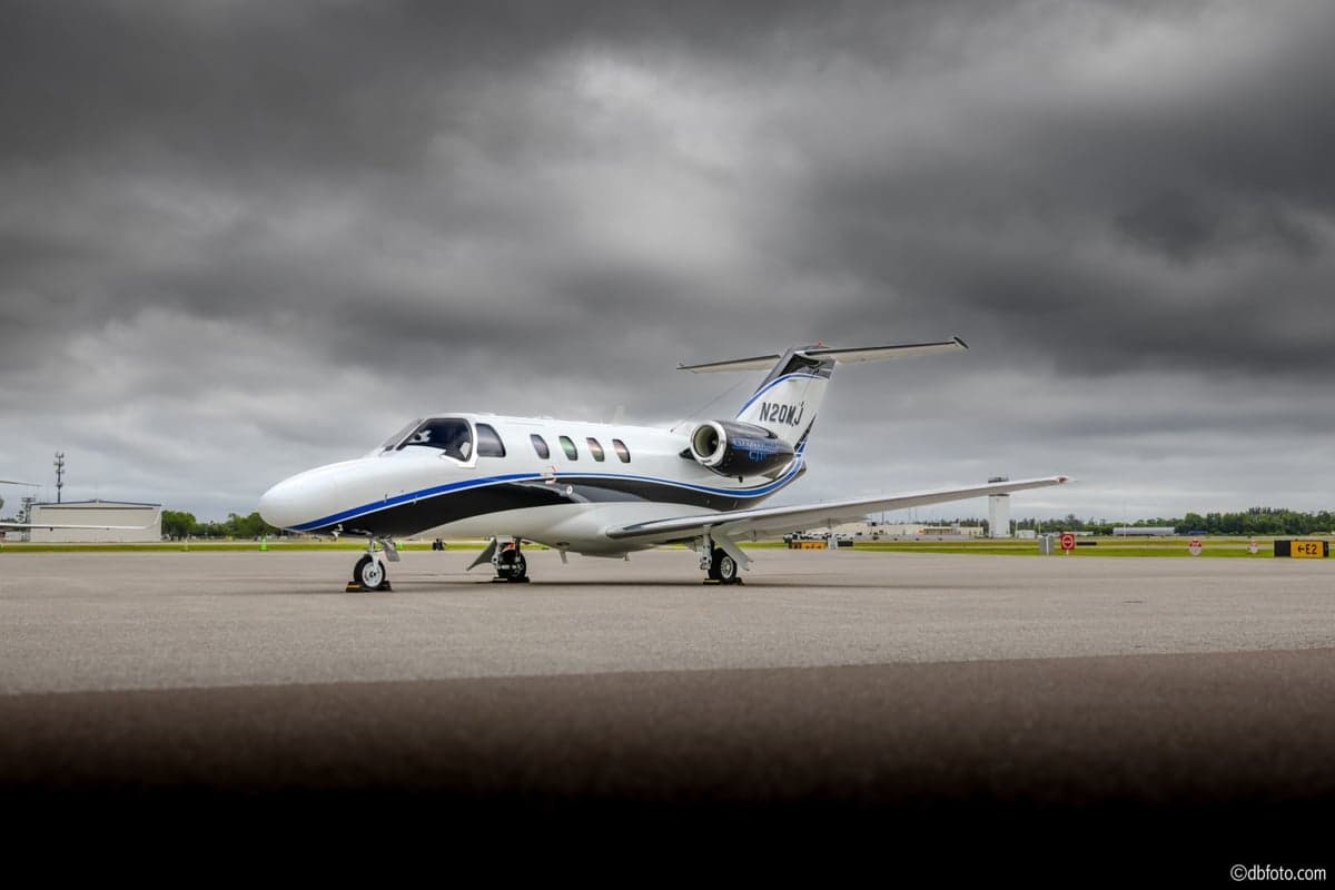 A Citation CJ aircraft with registration N20MJ is parked on the tarmac with a cloudy sky overhead.