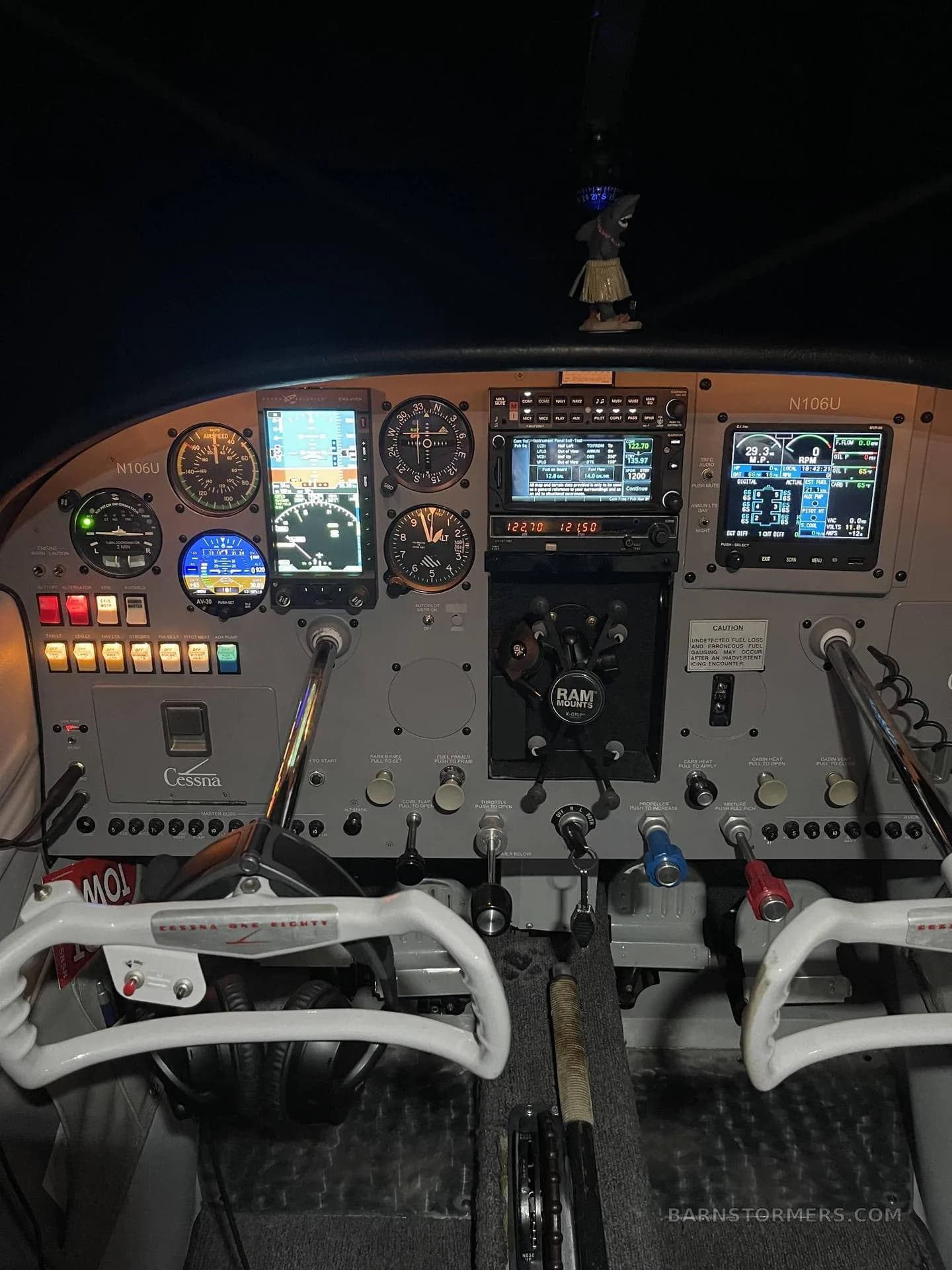 The illuminated cockpit of a Cessna 182 (N106U) features a modern avionics panel with multiple digital displays and traditional gauges.