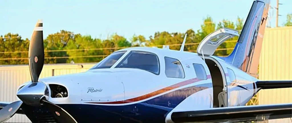 A close-up view of the front of a Piper Matrix N454CW aircraft with its passenger door open, parked on an airfield.