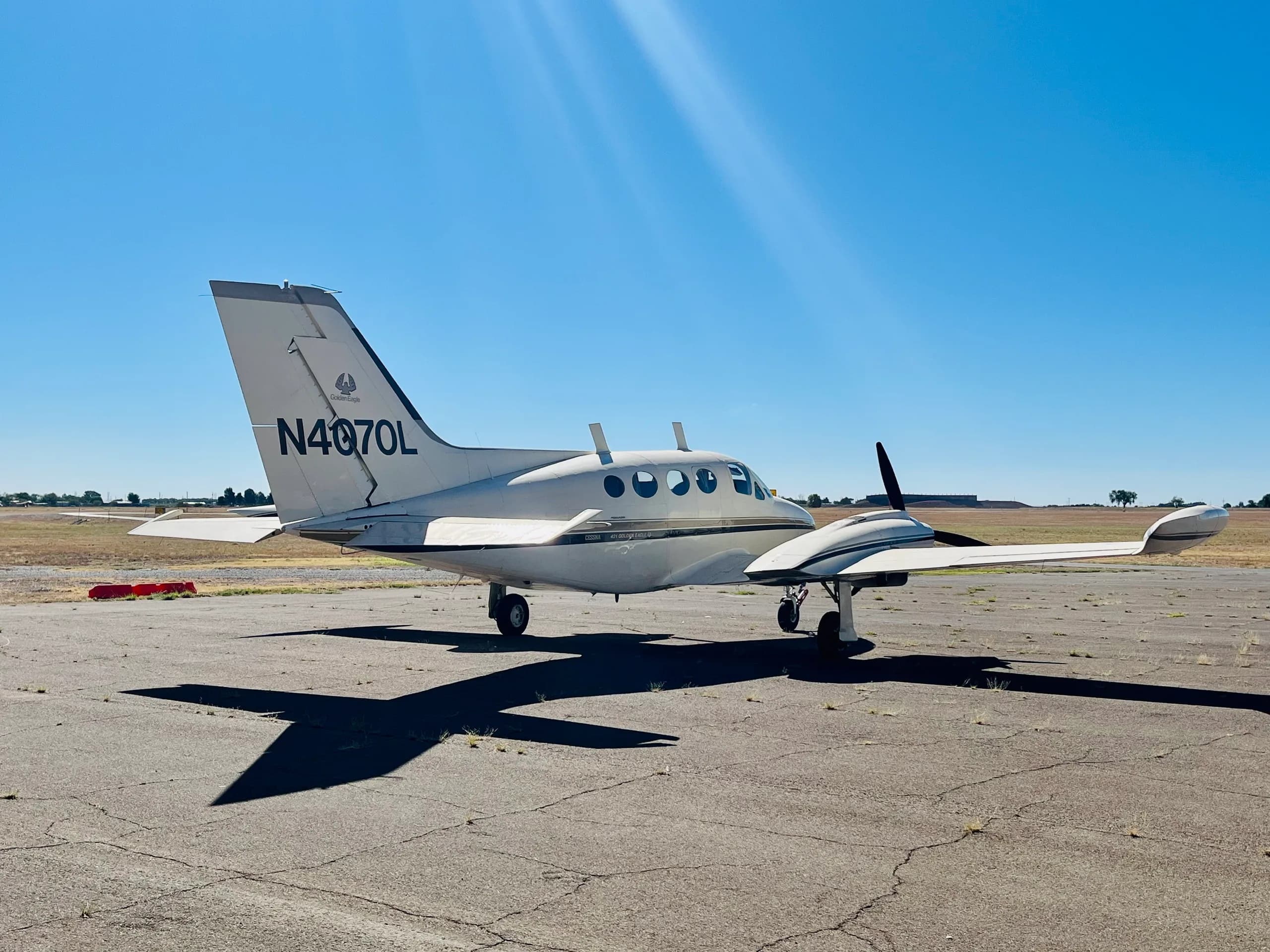 A three-quarter rear view of a white and gold Cessna 421 Golden Eagle (N4070L) parked on an airfield.