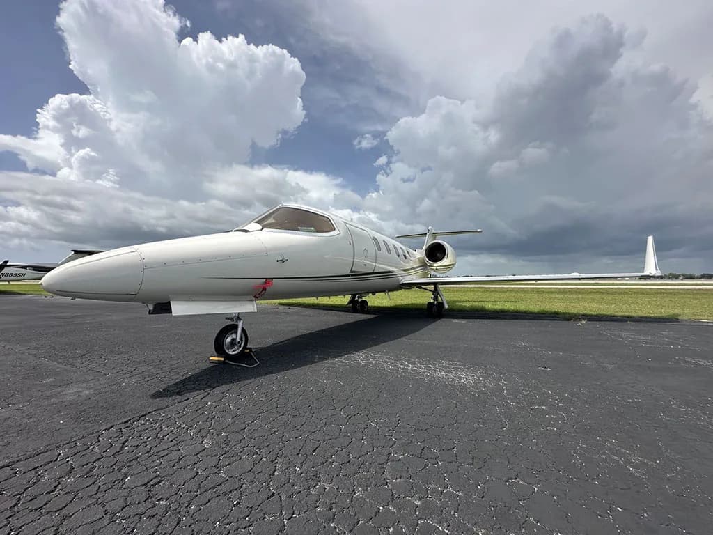 A white Learjet 35A with green and gold stripes parked on an asphalt ramp under a cloudy sky.