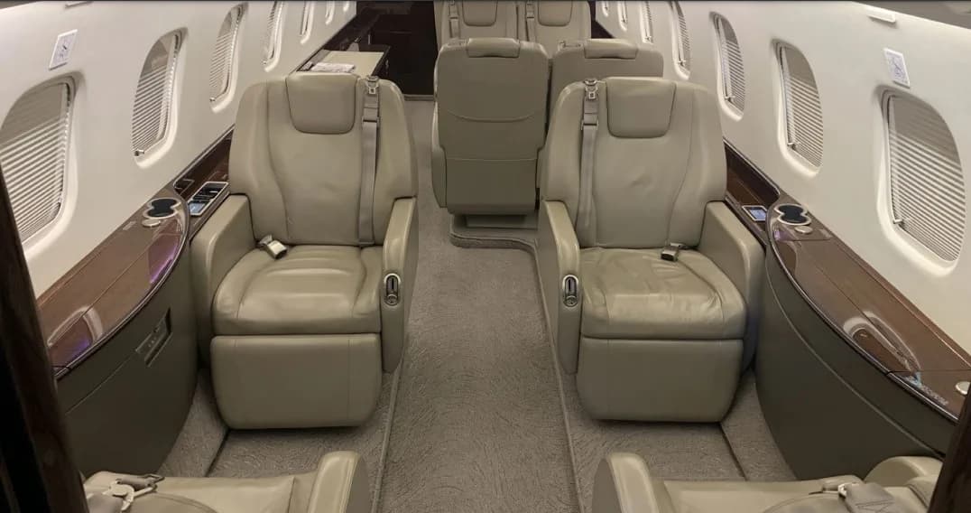 A view down the aircraft cabin aisle, showing two rows of beige leather seats and dark wood paneling.