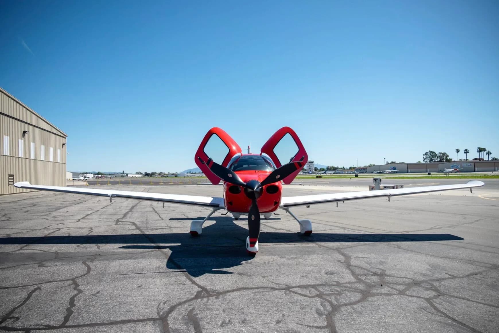 Front view of a red and white single-engine aircraft with its doors open on an airfield.