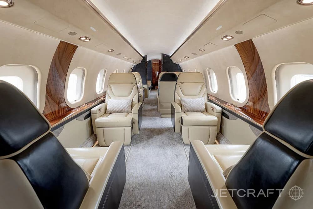 The luxurious cabin interior of a Bombardier Global business jet, showing rows of beige leather seats and wood paneling.