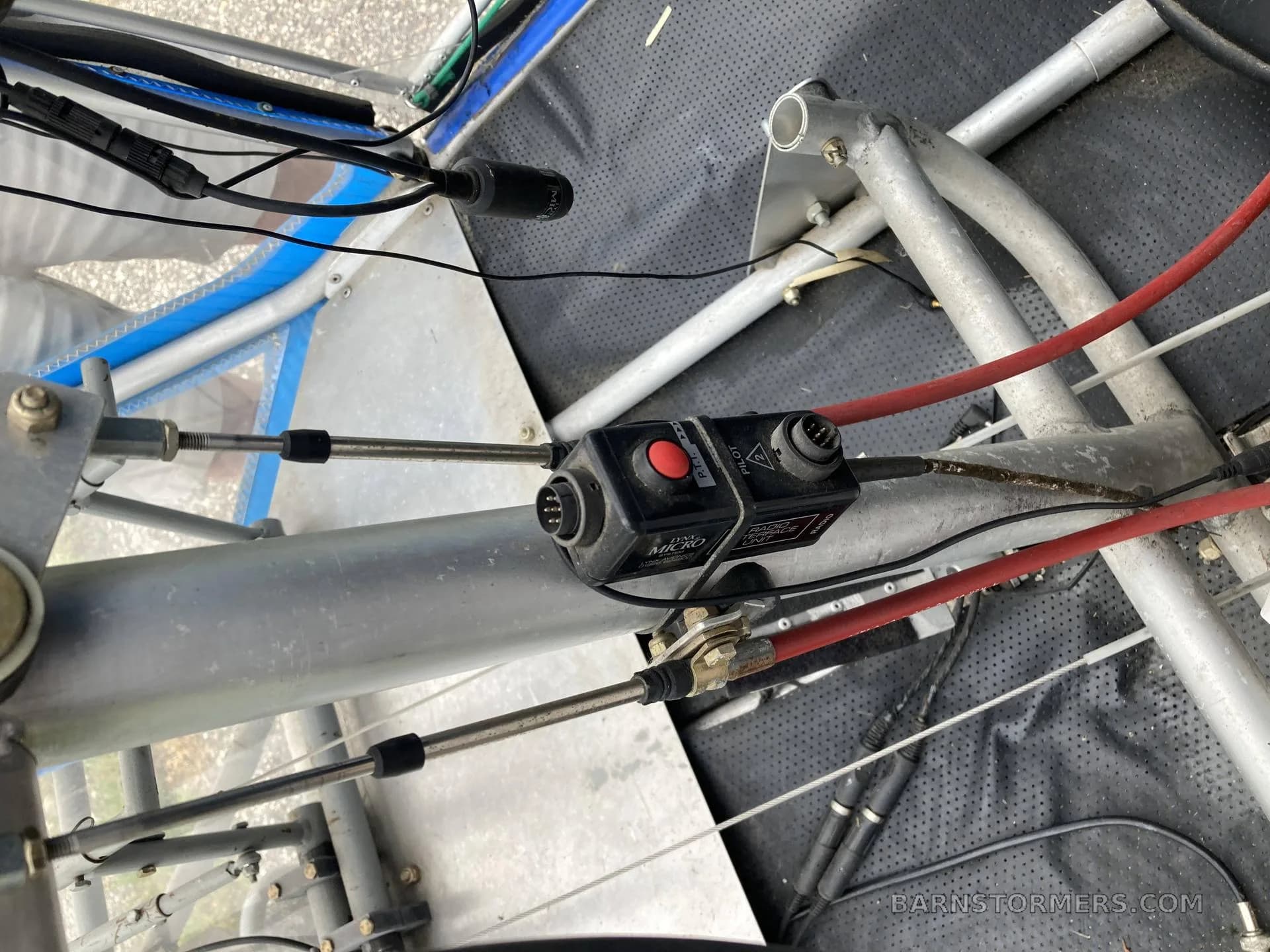 A close-up view of internal aircraft wiring, control cables, and a black electronic module with a red button.