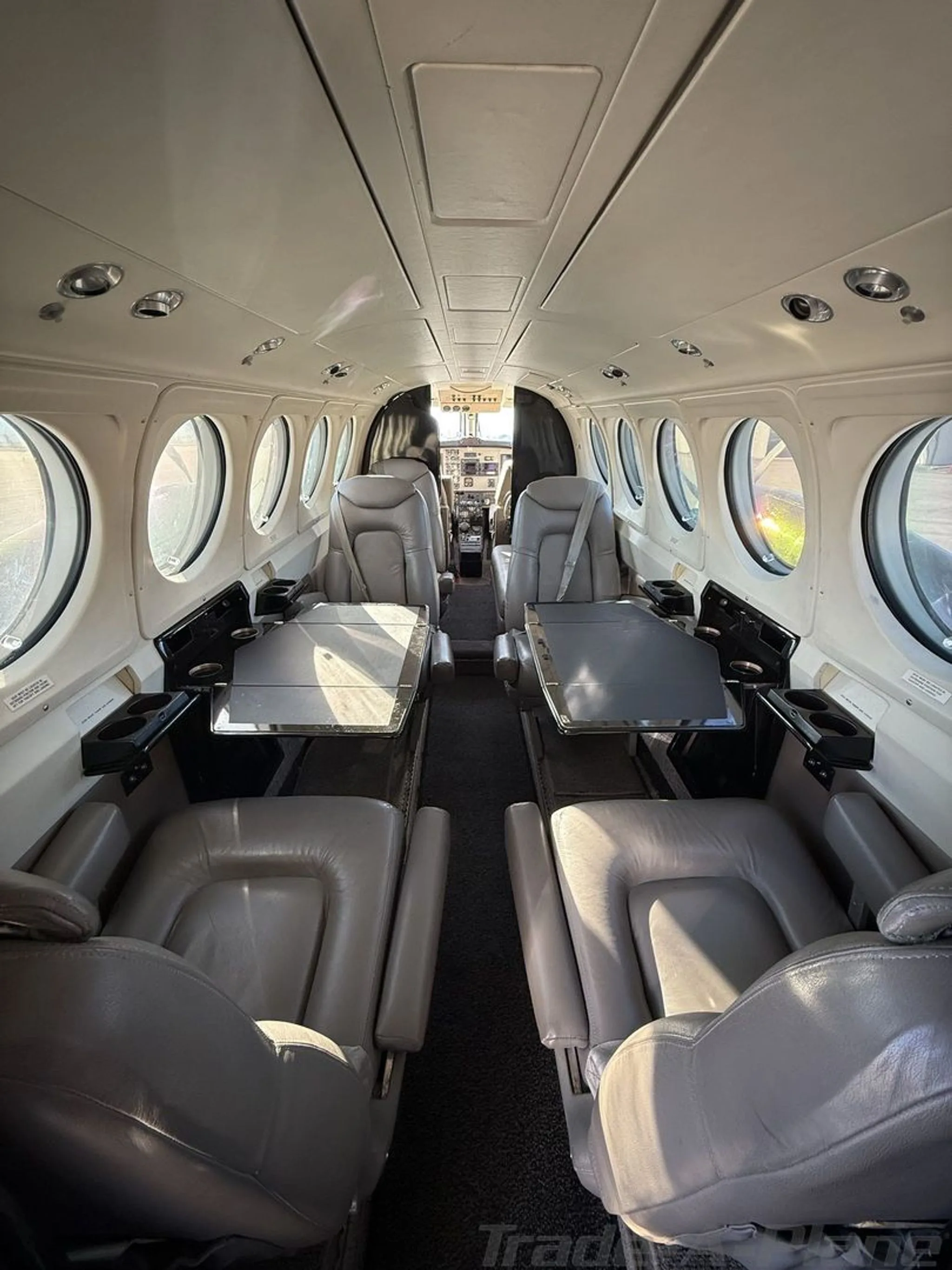 The interior cabin of a Beechcraft King Air 200, featuring grey leather seats and fold-out tables.