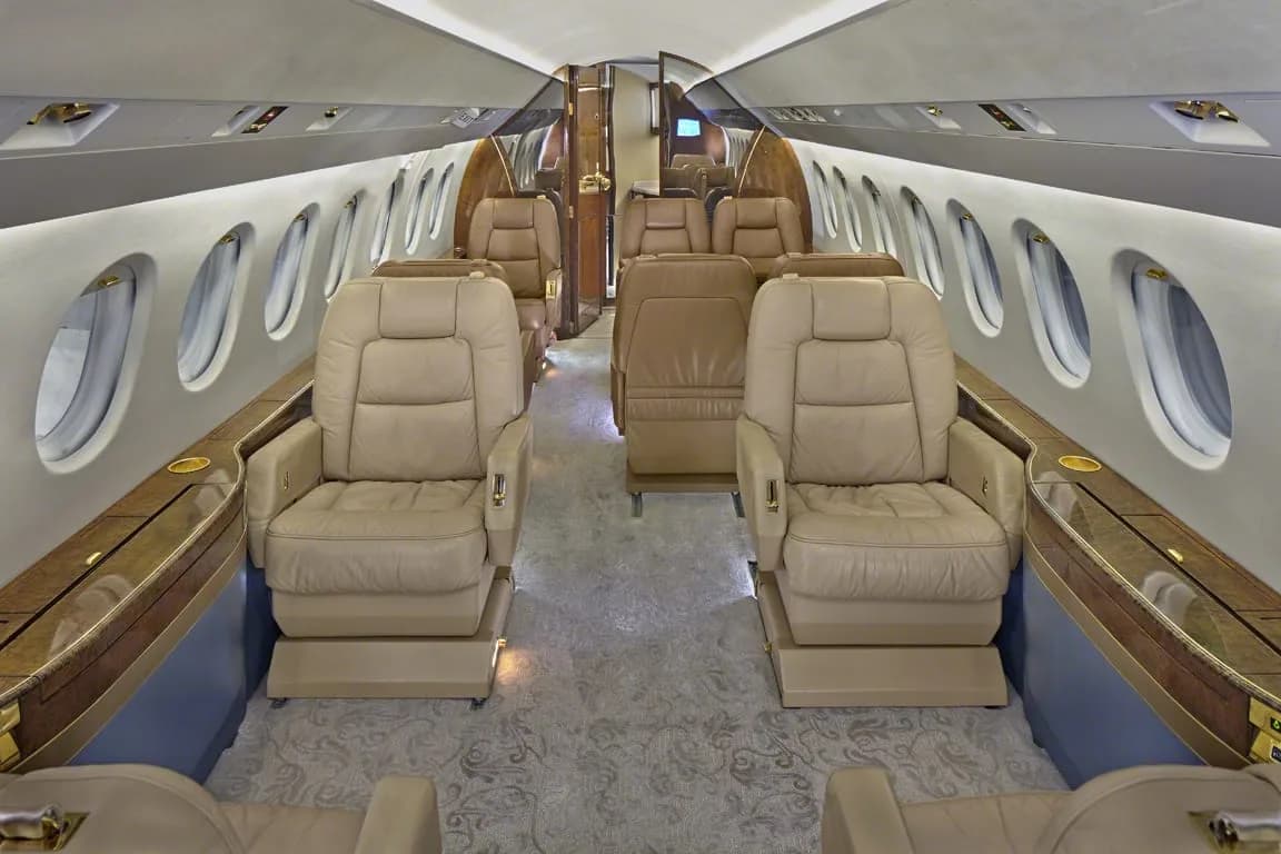 The luxurious cabin interior of a private jet with beige leather seats and a wooden table.