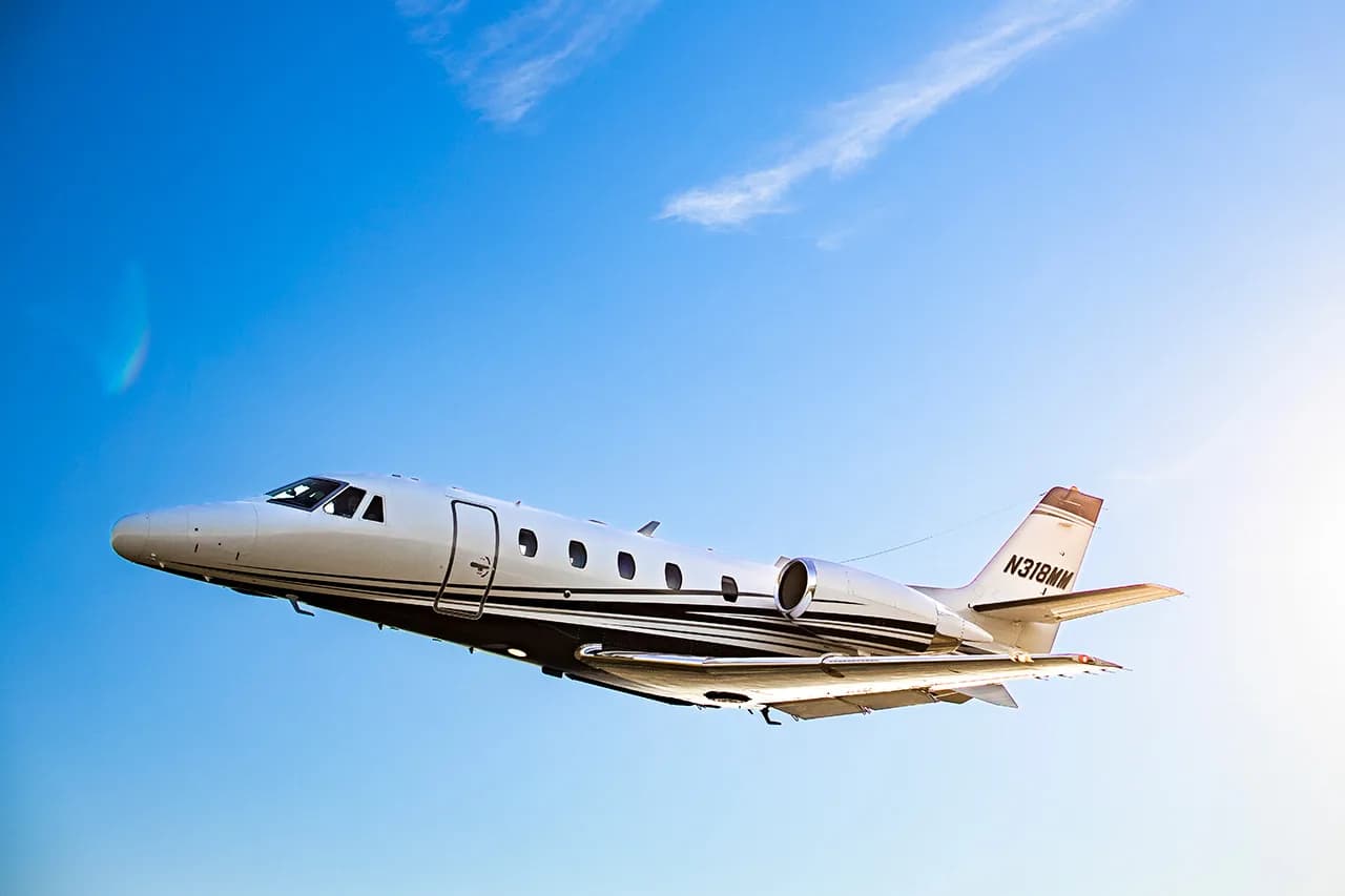 A Cessna Citation CJ3 aircraft, registration N318MM, is shown in flight against a blue sky.