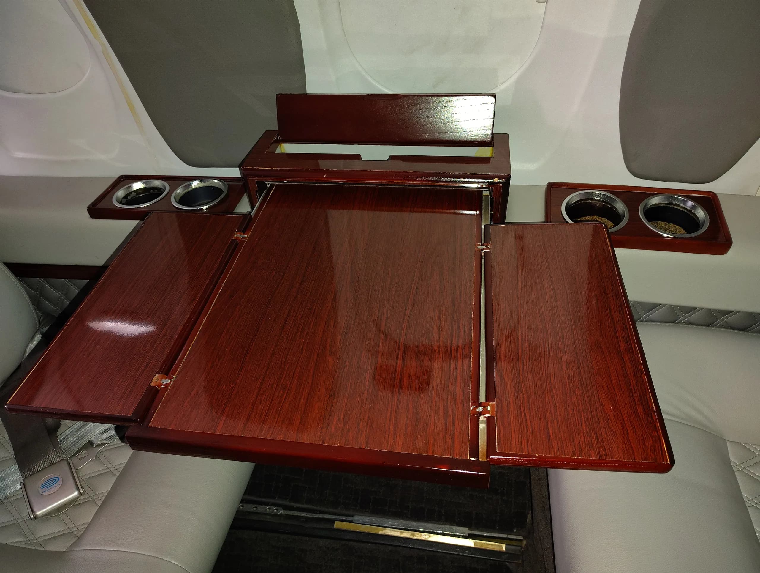 A close-up view of a polished wooden fold-out table and cup holders in an aircraft cabin.