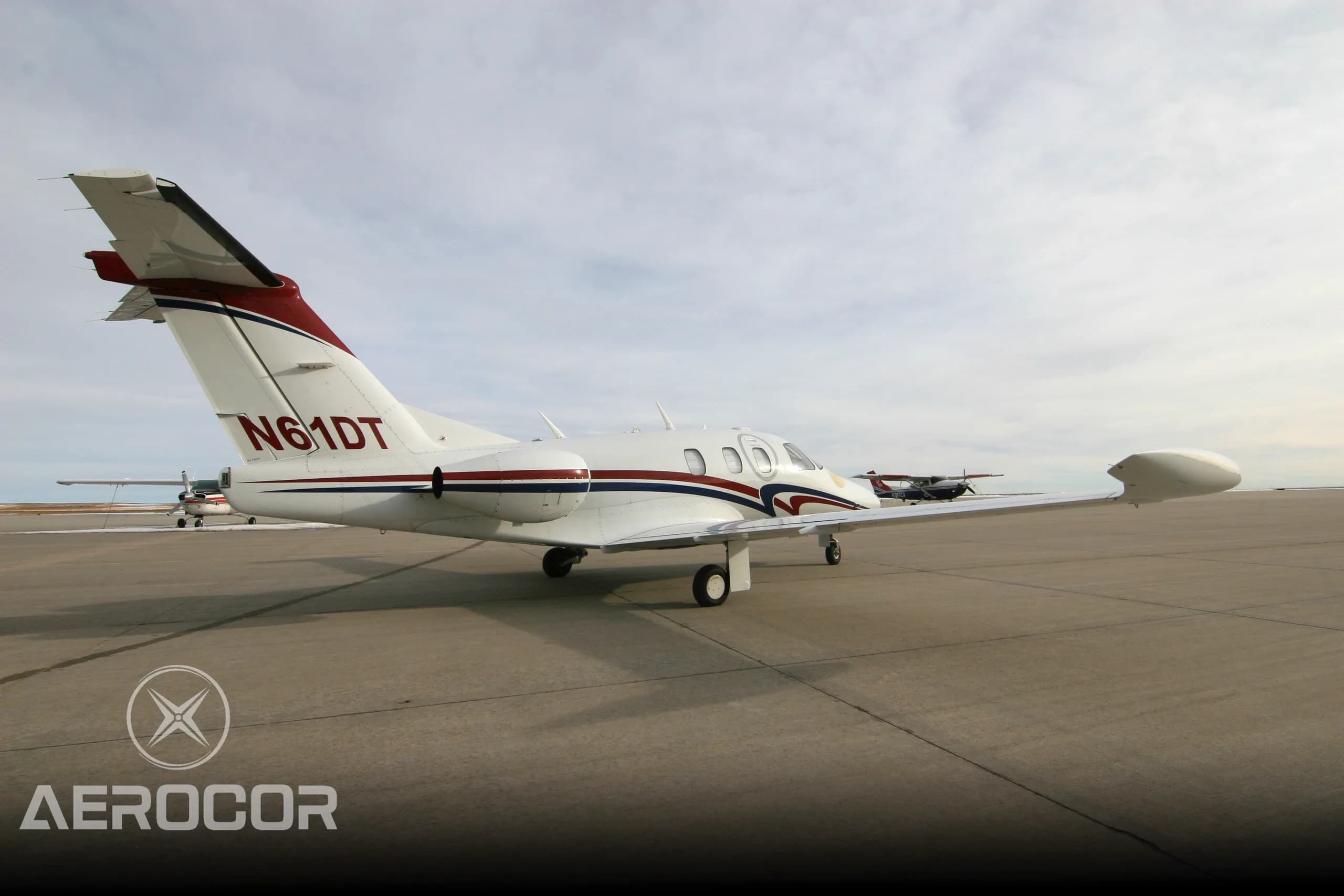 A white Eclipse 500 jet with red and blue stripes parked on an airport tarmac, viewed from the rear-right.