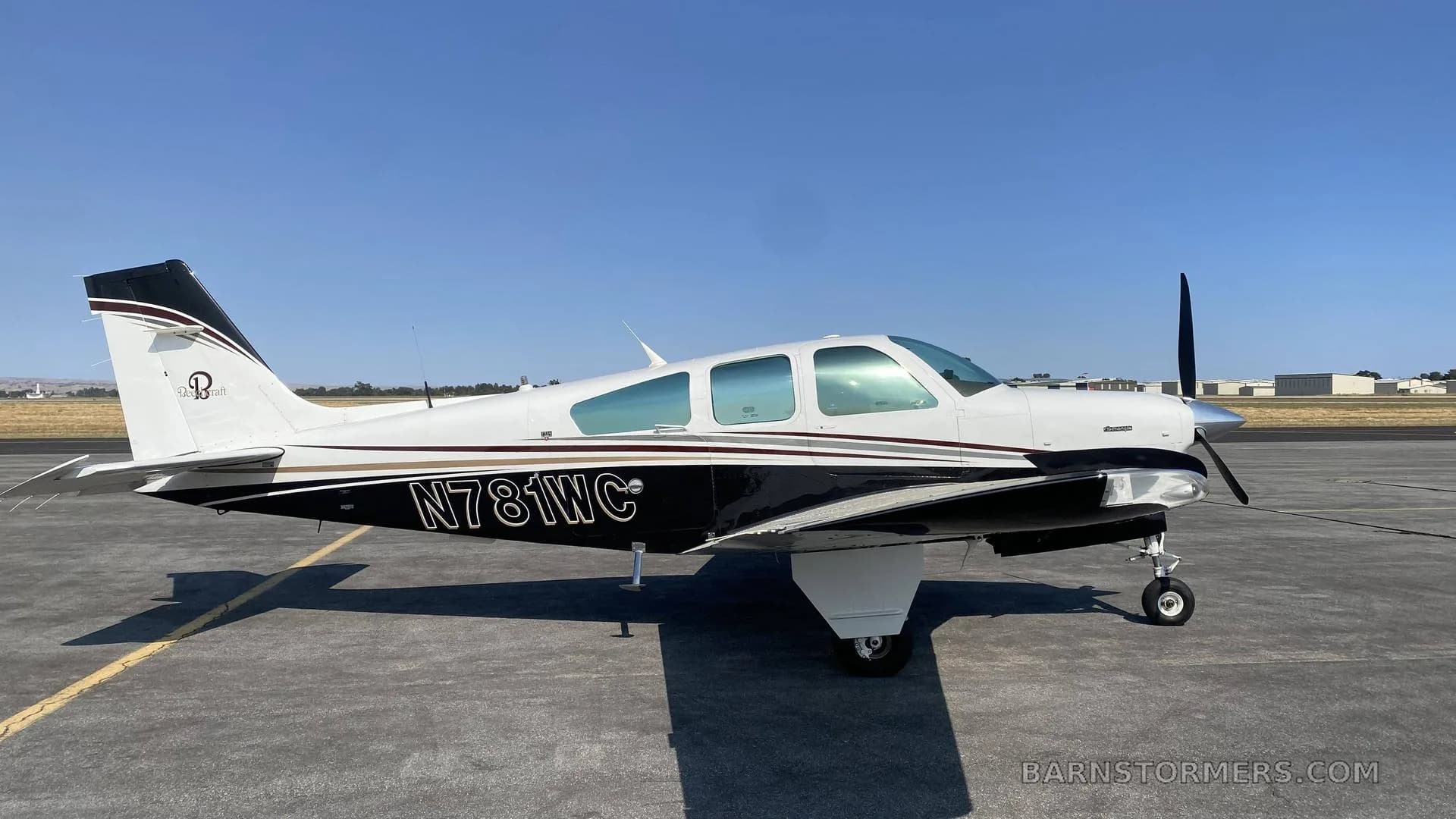 A side view of a white and black single-engine aircraft with registration N781WC, parked on an asphalt tarmac.