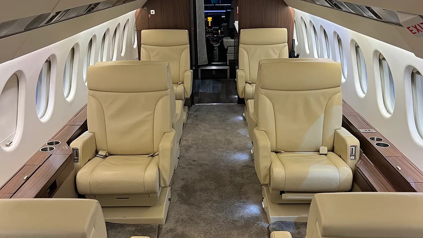 A view down the aisle of an aircraft cabin showing multiple beige leather executive seats.
