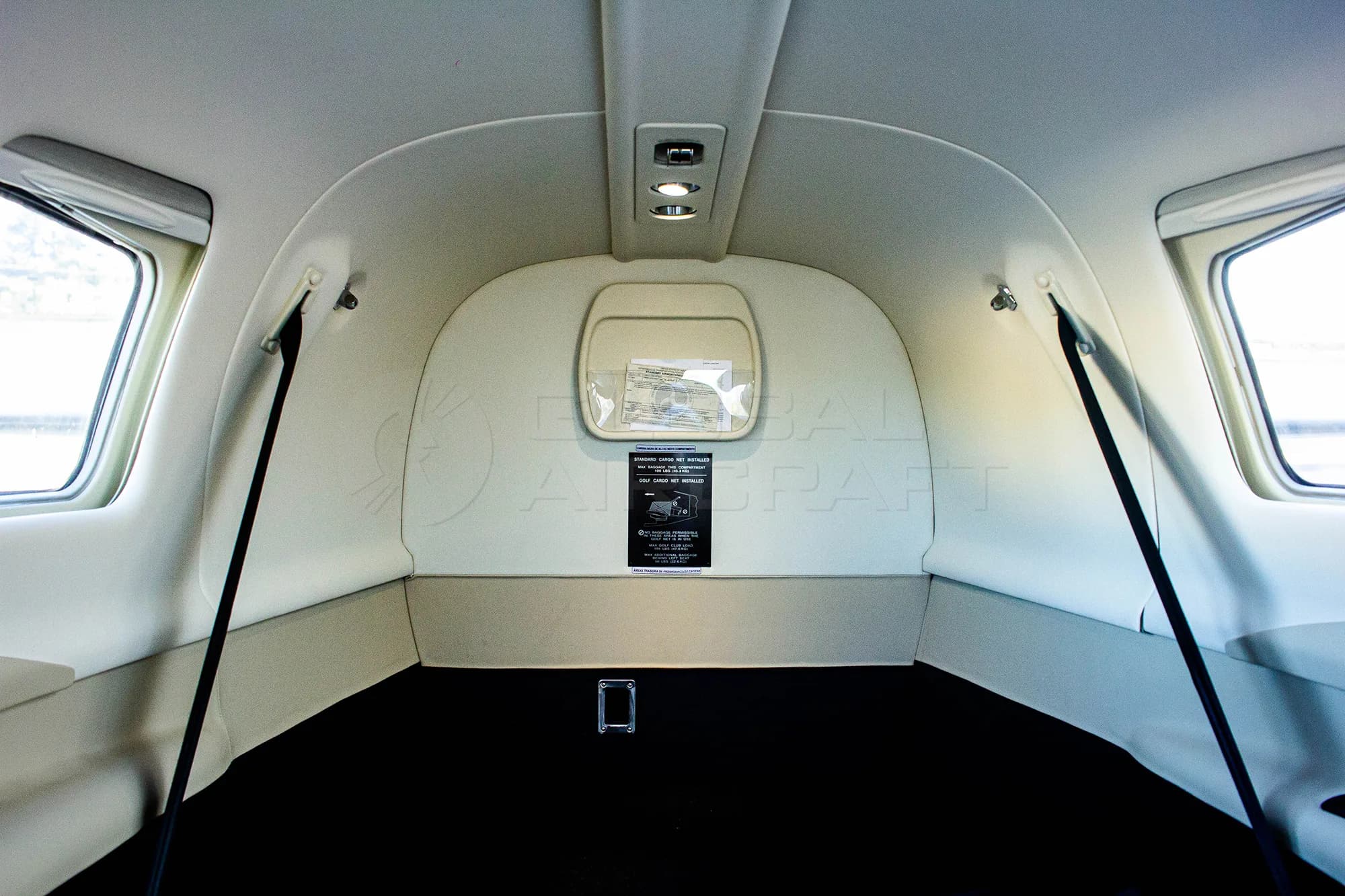 The rear cargo area of an aircraft cabin, featuring a black floor and light-colored walls with windows.