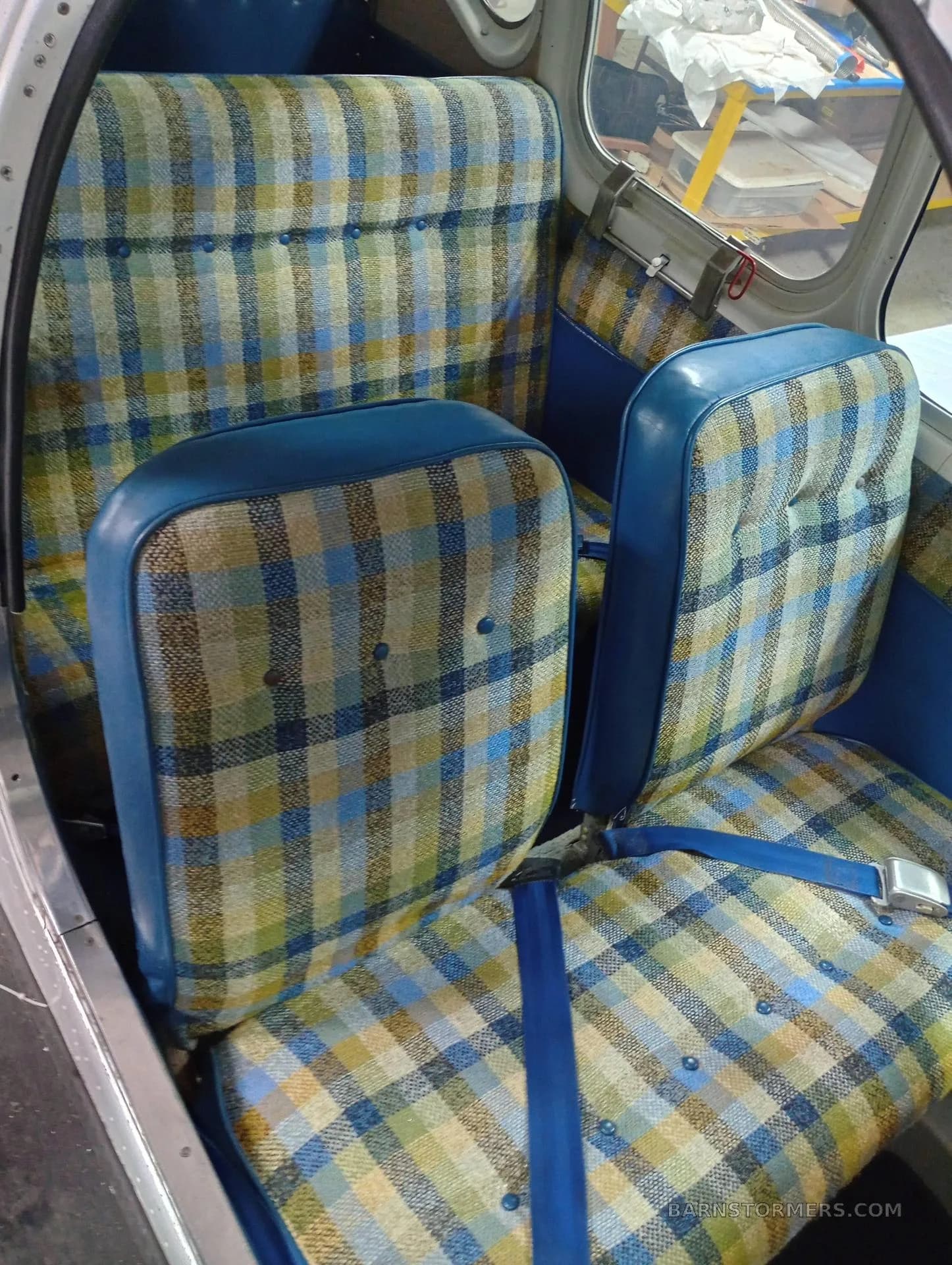 The aircraft's interior showing blue and plaid patterned seats with blue seatbelts.