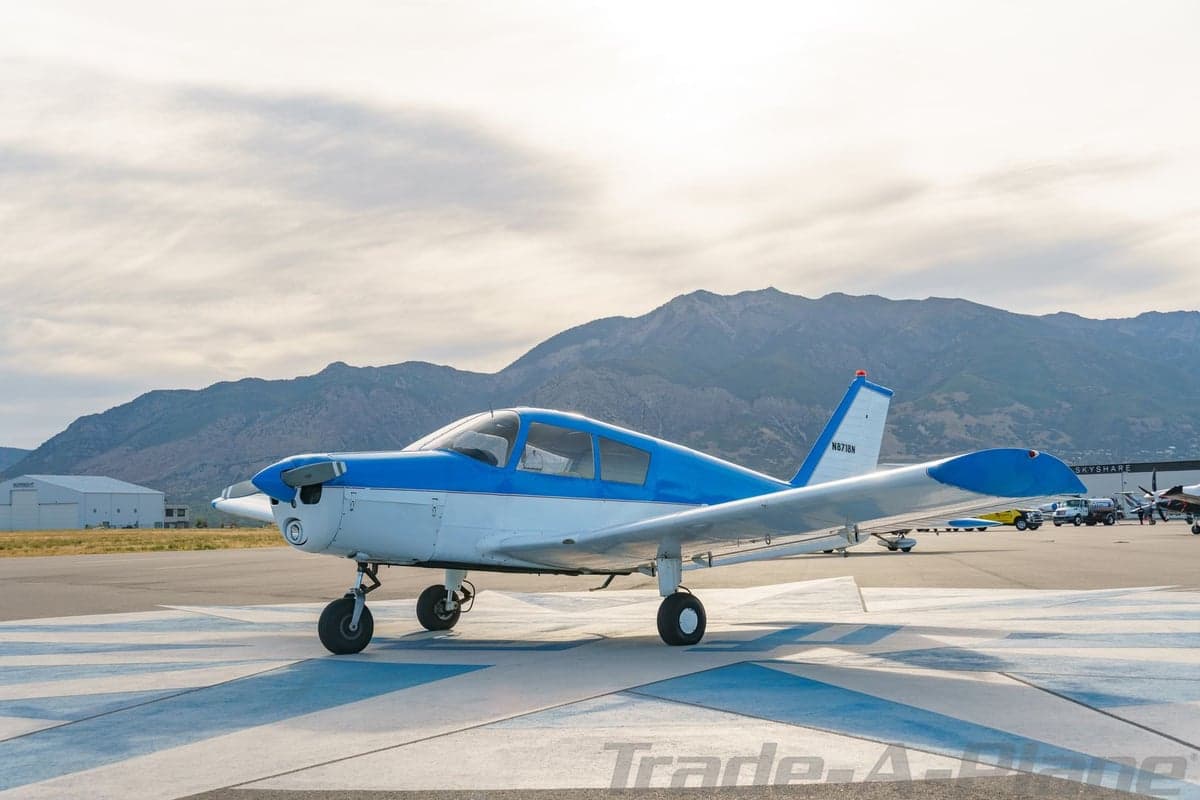 A three-quarter front view of the blue and white single-engine aircraft N8718N on a patterned tarmac with mountains in the distance.
