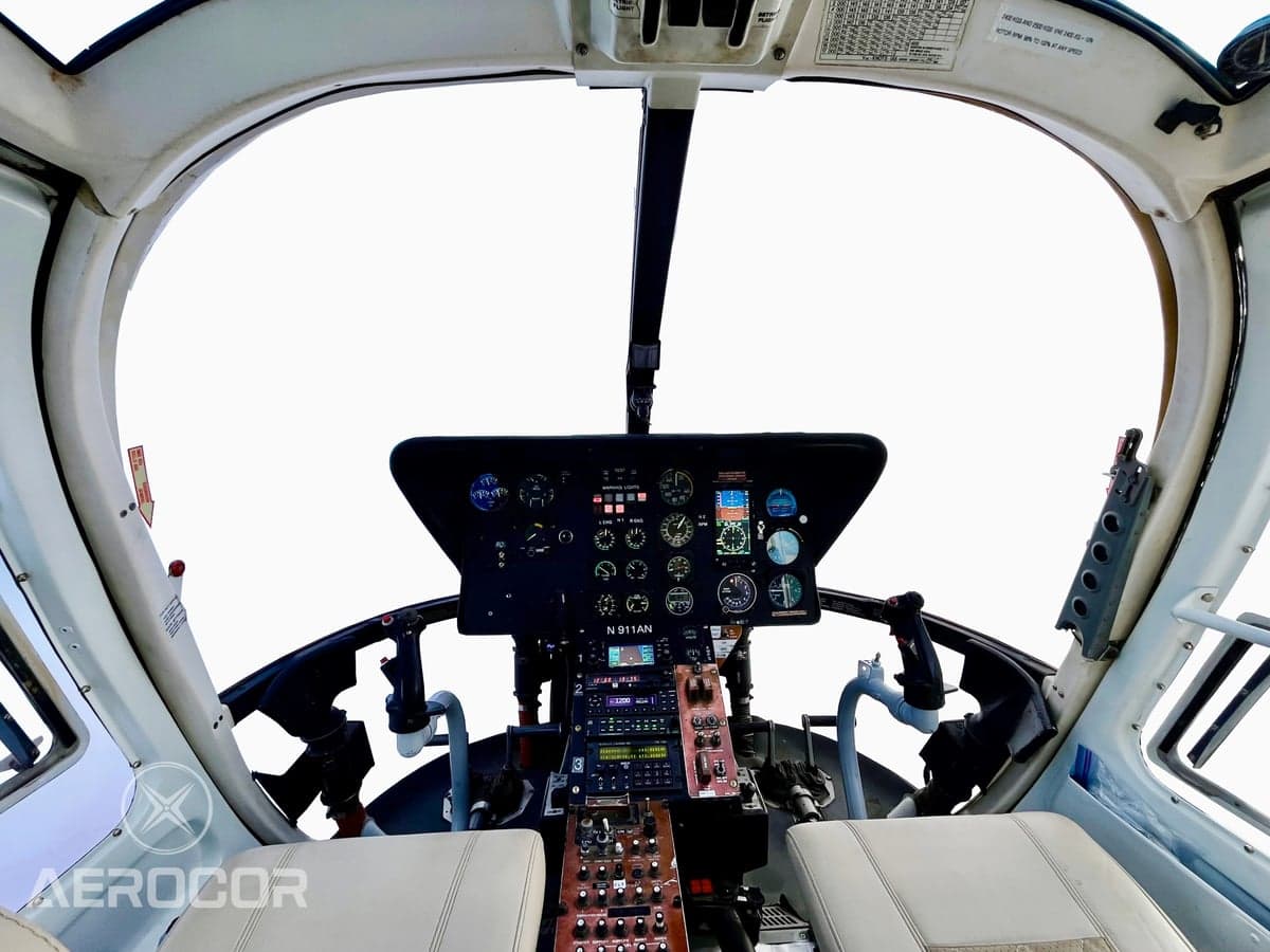 A wide view of the helicopter cockpit, showing the instrument panel, controls, and front seats.