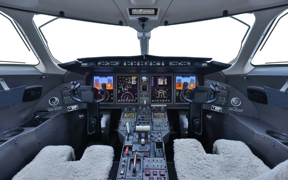 The modern cockpit features multiple digital displays, a complex control panel, and two pilot seats with sheepskin covers.