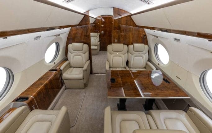 Aircraft cabin interior with leather seats and wood trim.