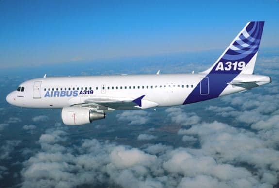 A white and blue Airbus A319 flies through the clouds.