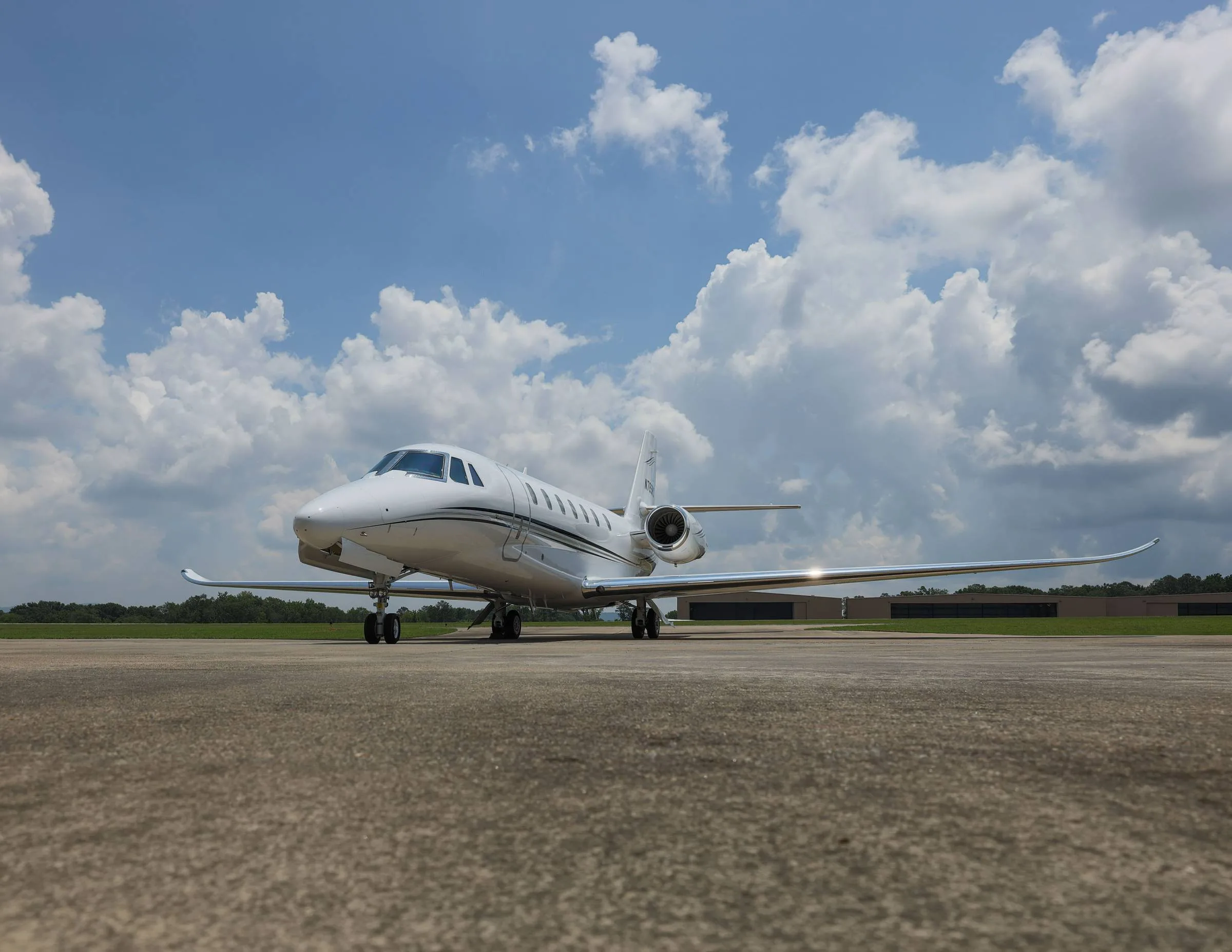 A low-angle front-side view of a white business jet with black stripes on an airfield.