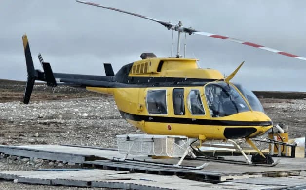 A yellow and black Bell 206 helicopter is parked on a wooden platform.