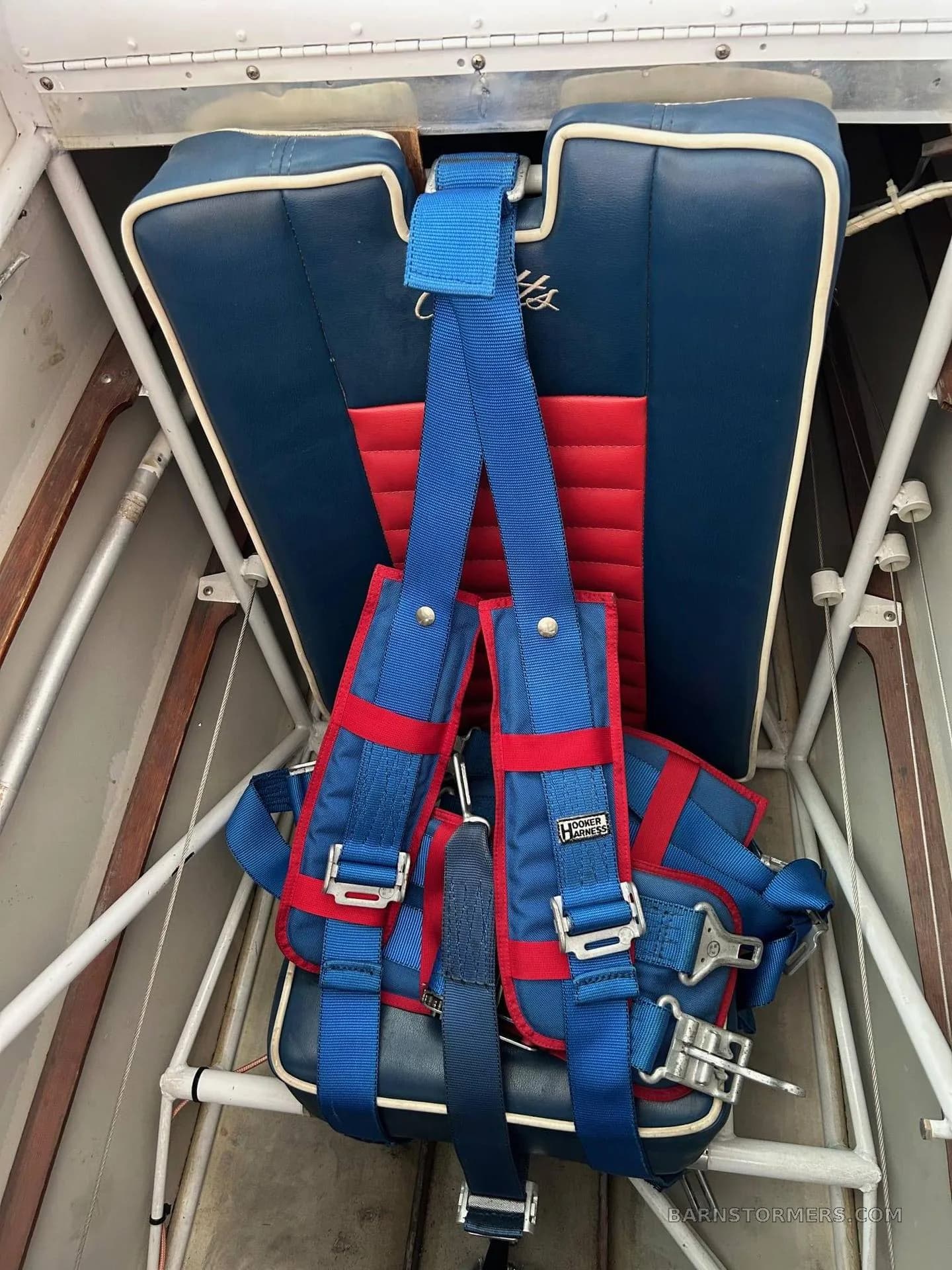 A blue and red aircraft seat with a multi-point harness, visible inside the cockpit or cabin structure.