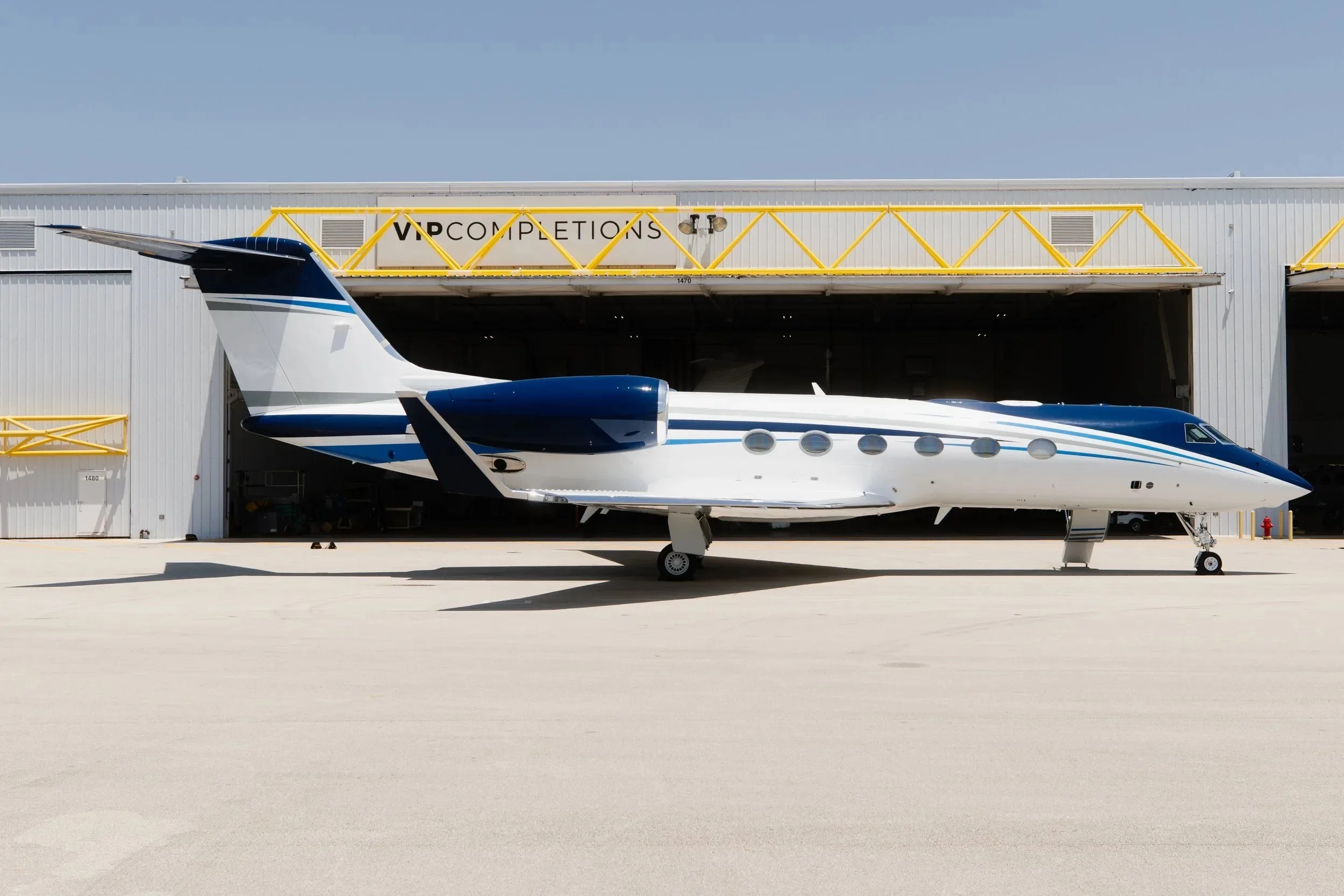 A side view of a white and blue Gulfstream G550 business jet parked in front of a hangar.