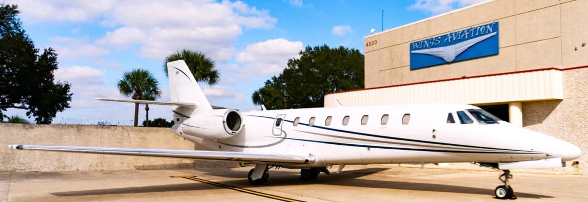 A white jet aircraft is parked in front of the Wings Aviation building.