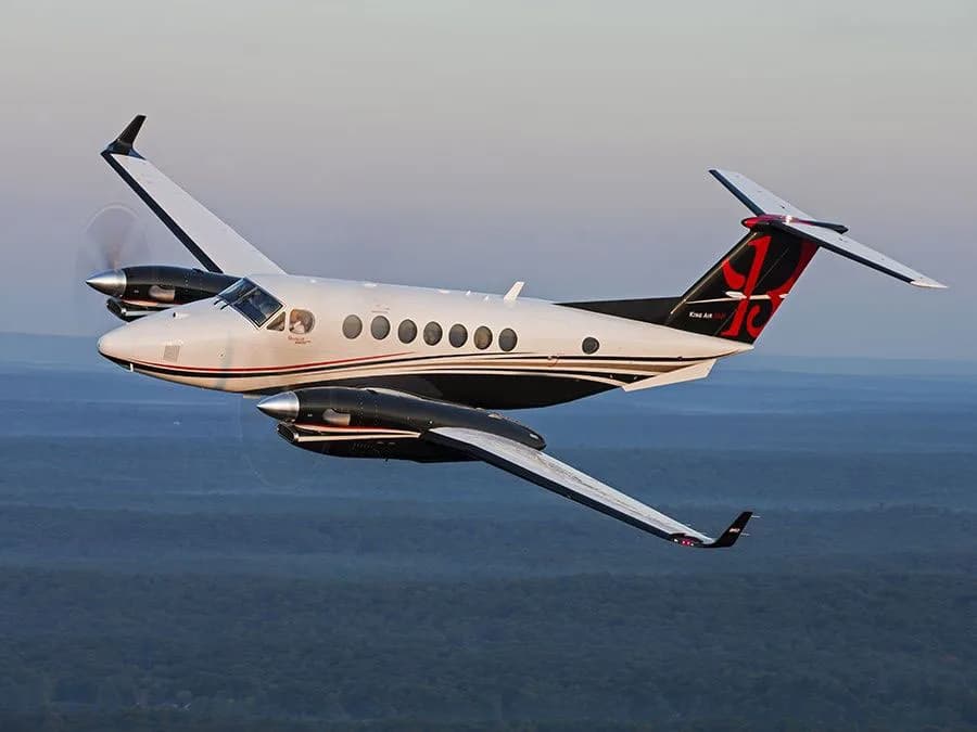 King Air 350 in flight over a wooded area.
