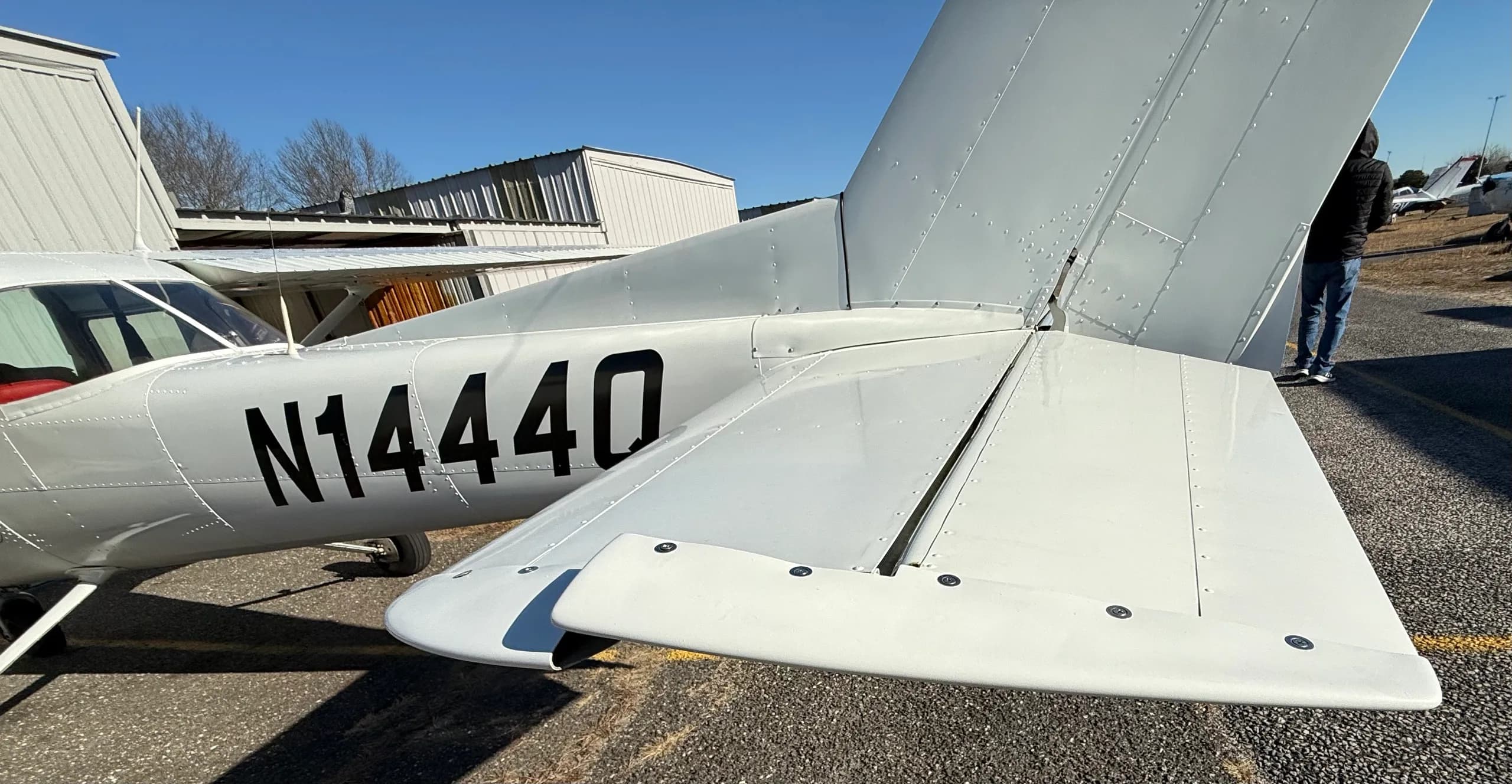 A rear-side view of the white Cessna 150 aircraft, showing the tail, horizontal stabilizer, and registration N1444Q.