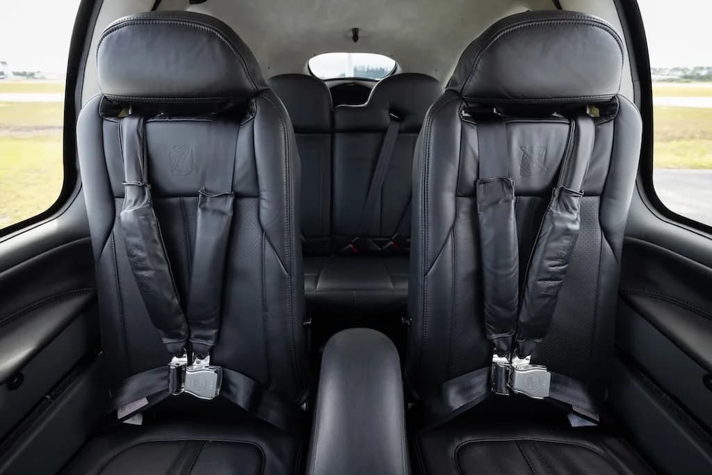 The black leather front seats of a Cirrus SR20 aircraft cabin, with seatbelts visible.