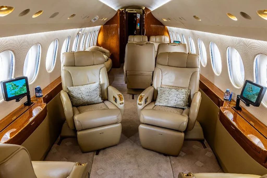 The spacious private jet cabin featuring tan leather seats, individual screens, and polished wood tables.