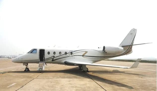 A white Cessna Citation business jet with gold and black stripes on the tarmac, with its door open and stairs extended.